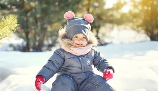 Bébé en combinaison assis dans la neige et souriant