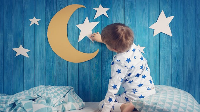 enfant au lit étoiles et lune en papier sur mur