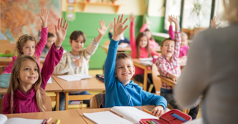 enfants qui lèvent la main assis dans une salle de classe