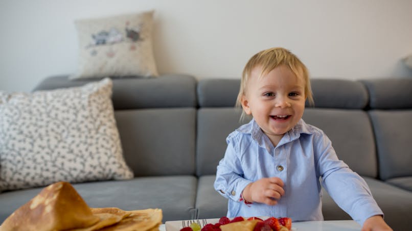 Bébé qui rigole à côté d'une assiette de crêpes.